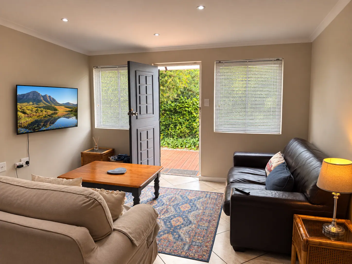 Lounge with television, leather sofa, and open door to the deck